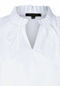 Chemisier blanc avec un col plissé, un design en V et une texture lisse. L'étiquette indique "MORE&MORE" et la taille 36.