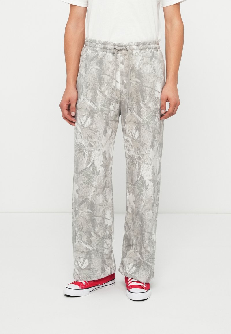 Light gray, floral-patterned sweatpants with an elastic waistband and drawstring. Paired with red low-top sneakers.
