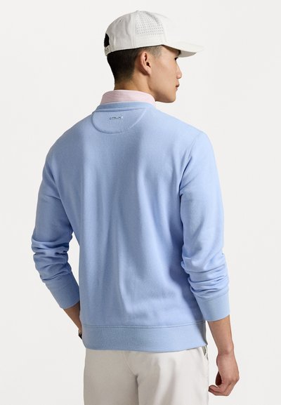 Pull léger bleu en tricot fabriqué dans un tissu doux, avec des poignets et un ourlet côtelés, et un col contrastant. Détail de logo discret au niveau du col.