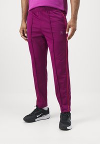 Pantaloni sportivi di un vivace magenta con strisce laterali nere e rosse, dotati di una vita elastica e una trama liscia.