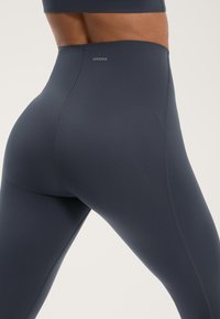 Hög midjas leggings i mörkgrått tyg med en mjuk yta. Har en subtil logotyp och rena sömsdetaljer.