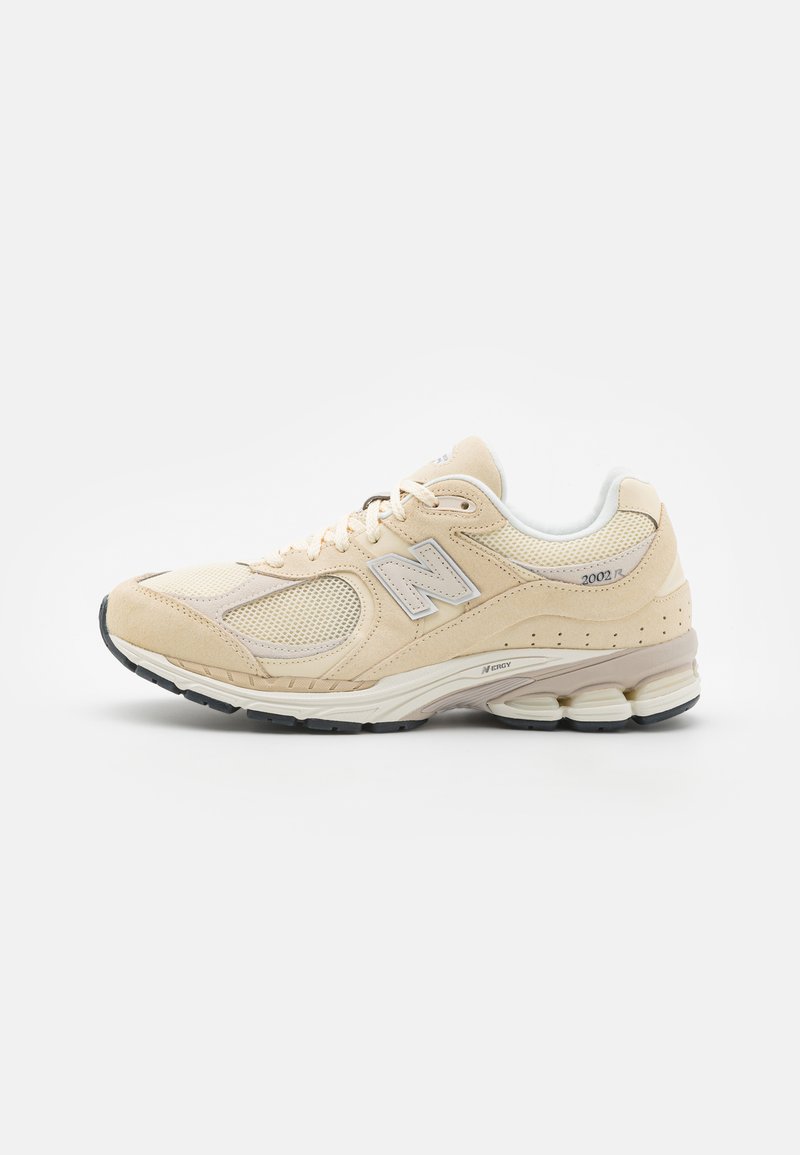 Scarpa da ginnastica beige con tomaia in suede e mesh, dettagli bianchi, suola testurizzata e logo N prominente sul lato. Presenta un collare imbottito.