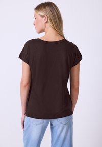 Maglietta a maniche corte marrone con scollatura ampia e vestibilità rilassata. Tessuto liscio, con spacchi laterali e senza motivi o dettagli visibili.