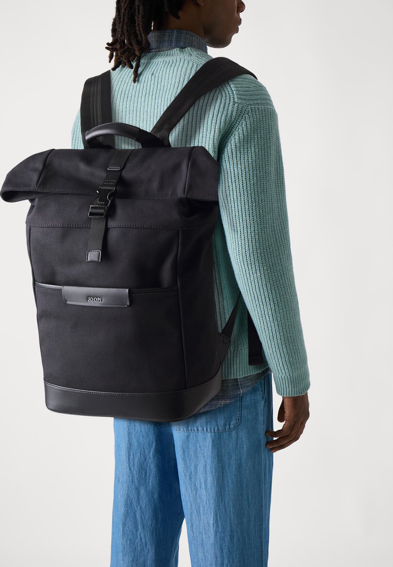 Mochila negra tipo roll-top con correas ajustables, bolsillo lateral y detalles en cuero. Tela de superficie texturizada para mayor durabilidad.