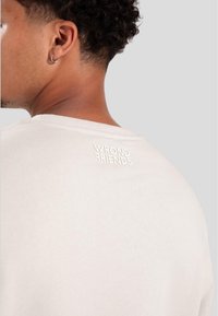 Light beige cotton t-shirt featuring a round neck and stitched text "WRONG FRIENDS" on the upper back, smooth texture.