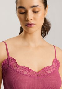 Fuchsia ribbed camisole with lace trim at the neckline and thin adjustable straps. Soft texture, fitted design, and floral lace accents.