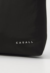 Svart treningsbag laget av glatt, matt stoff; har en hvit "CASALL" logo på siden; rektangulær form med myke kanter.