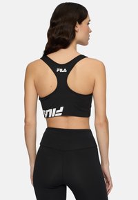 Czarny stanik sportowy z designem typu racerback, z białym logo FILA na plecach i krojem w stylu cropped, w zestawie z czarnymi legginsami o wysokim stanie.