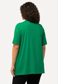 Zielona koszulka z krótkim rękawem, okrągłym dekoltem, luźnym fasonem, wykonaną z miękkiej bawełny o gładkiej fakturze. Widoczne detale szwów z tyłu.