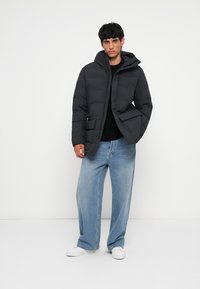 Black puffer jacket with a hood, featuring a zip front and large side pockets. Paired with loose light-wash jeans and white sneakers.
