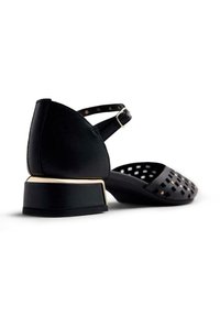 Sandalias de tacón negro con punta abierta, que presentan un diseño recortado en la parte superior y un detalle dorado en el tacón cuadrado. Incluye una correa de tobillo ajustable.