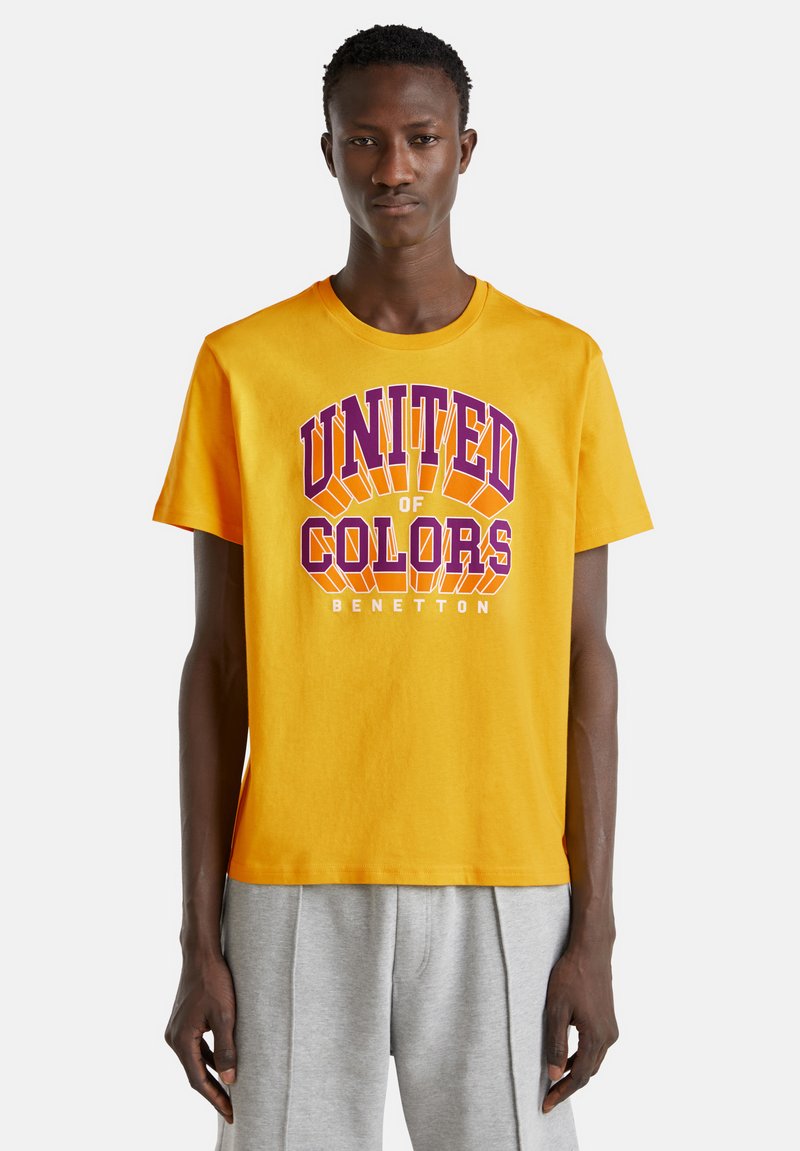 Žluté bavlněné tričko s textem "UNITED of COLORS" v purpurové a oranžové barvě, s volným střihem a krátkým rukávem.