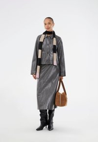 Veste en cuir gris avec une finition brillante, jupe grise assortie, bottes noires montantes, écharpe multicolore et sac à main marron.