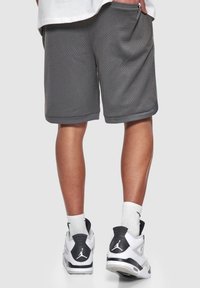 Shorts de sport gris en tissu en maille respirante, avec des poches latérales et une coupe décontractée. Assortis avec des baskets blanches et noires.