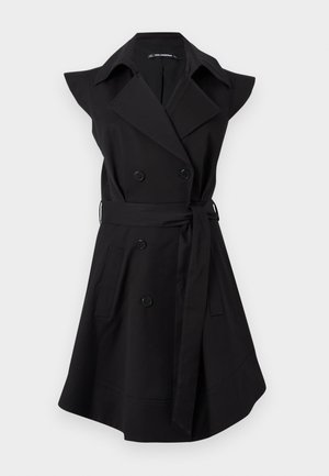 Robe trench-coat noire sans manches, croisée, avec col large, poches latérales et ceinture à nouer à la taille, sur fond blanc.