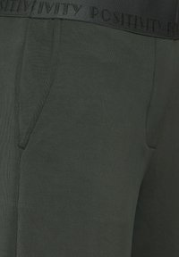 Donkergroene joggers van een gladde katoenmix. Beschikt over een dikke elastische tailleband met de opdruk "POSITIVITEIT" en zijzakken.