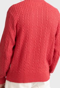 Pull rouge en tricot avec motif torsadé, poignets côtelés et ourlet côtelé. Tissu texturé avec une coupe décontractée et un col arrondi.