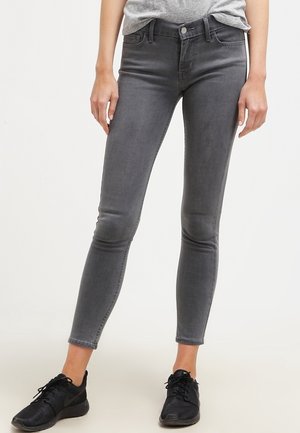 Jeans skinny grises de denim, con un talle medio, diseño de cinco bolsillos y un sutil acabado desvanecido. Zapatillas deportivas negras complementan el conjunto.