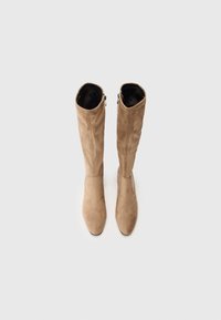 Bottes en suède beige montantes, avec une texture lisse, des bouts pointus et des zips sur les côtés extérieurs pour un enfilage facile.
