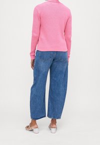 Růžový pletený svetr s dlouhými rukávy, ve spojení s volně střiženými modrými džínami. Sandály mají silný podpatek a ozdobné popruhy.