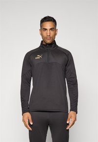Sudadera deportiva negra con media cremallera, con un alto cuello, logo en dorado y paneles en contraste en los hombros. Confeccionada con una tela suave.