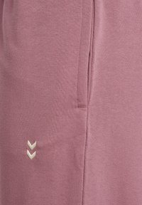 Hellrosa Sweatpants aus weichem Stoff, mit einer Seitentasche und einem in Cremefarbe bestickten Logo. Schlichtes, sauberes Design.