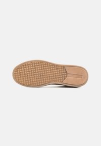 Semelle de chaussure en caoutchouc beige avec une surface texturée et un motif, ainsi qu'un léger talon. Comprend une découpe centrale pour plus de flexibilité.
