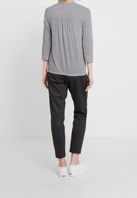 Top a maniche tre quarti con motivo bianco e nero, abbinato a pantaloni slim-fit a quadretti neri e scarpe da ginnastica bianche.