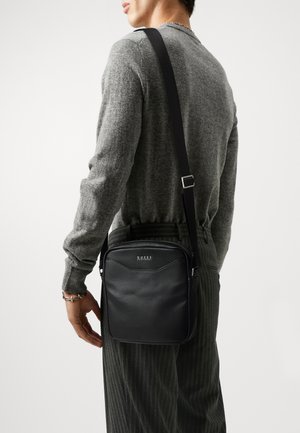 Borsa a tracolla in pelle nera con una texture liscia, forma rettangolare, tracolla regolabile e logo impresso sul davanti.