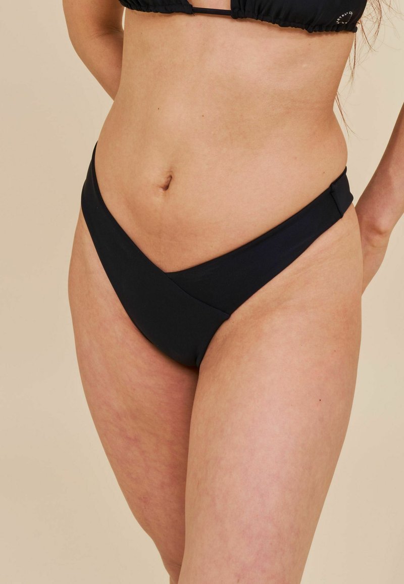 Juodas bikini apatinis trikotažas su V formos dizainu, lygia tekstūra ir šoninėmis akcento detalėmis, pasižymintis minimalia aprėptimi ir elegantišku siluetu.