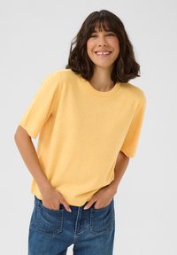 Pull à manches courtes, col rond, dans une teinte jaune clair, fabriqué à partir d'un tissu doux avec une texture subtile, associé à un jean en denim bleu.