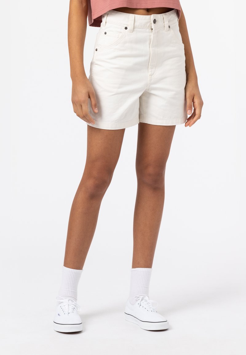 Pantaloni corti bianchi a vita alta in cotone con una texture liscia, dotati di chiusura con bottone frontale e tasche laterali. Abbinati a sneakers bianche.