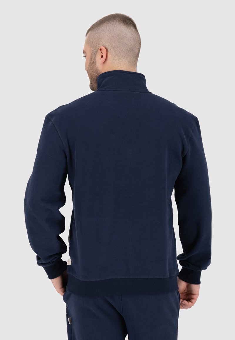 Marineblauwe fleece jas met een hoge kraag, lange mouwen en ribgebreide manchetten. Heeft een labeldetail aan de onderkant links.