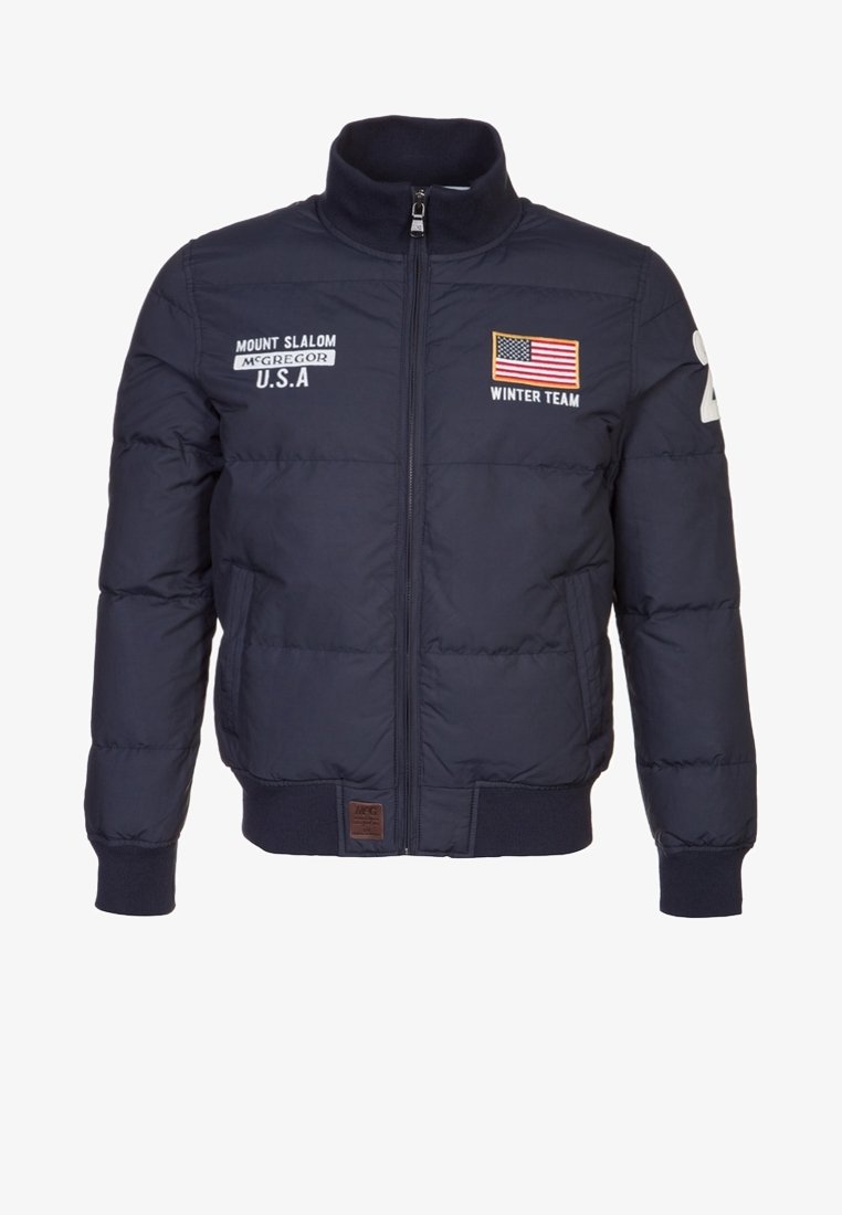 Navy puffer jacket with a high collar, front zipper, embroidered logos, U.S. flag, and ribbed cuffs. Features a padded design for warmth.