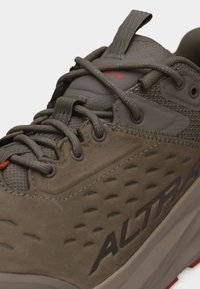 Κοντινό πλάνο καφέ παπουτσιού πεζοπορίας με υφή στο πλάι, στρογγυλά κορδόνια, θηλιά για τράβηγμα και ορατό λογότυπο «ALTRA» στη σόλα.