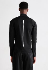 Mann sett fra bak, iført en svart langermet topp og bukser med en vertikal hvit stripe og "Calvin Klein"-tekst på ryggen.