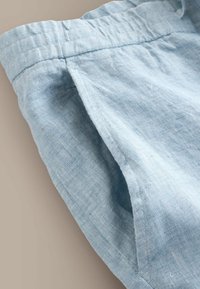 Pantalon en lin bleu clair avec taille élastique et poche latérale, présenté en gros plan sur un fond neutre.