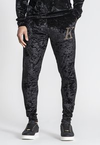 Zwarte fluwelen joggers met een aansluitend ontwerp, voorzien van een met rhinestones versierd "K"-logo op de bovenbeen en gecombineerd met zwarte veterschoenen.