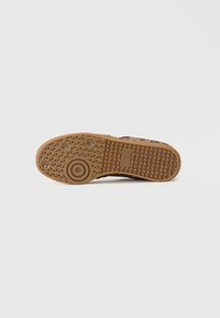Sola de sapato de borracha castanha com um design texturizado e padronizado. Apresenta padrões circulares e de aderência, com um destacado emblema da marca na lateral.