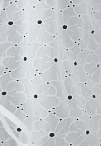 Λευκό κεντημένο ύφασμα με ανθικά σχ�έδια και μαύρα κέντρα. Η υφή είναι ελαφριά και αέρινη, συμπληρωμένη από μια ριμπόνα.