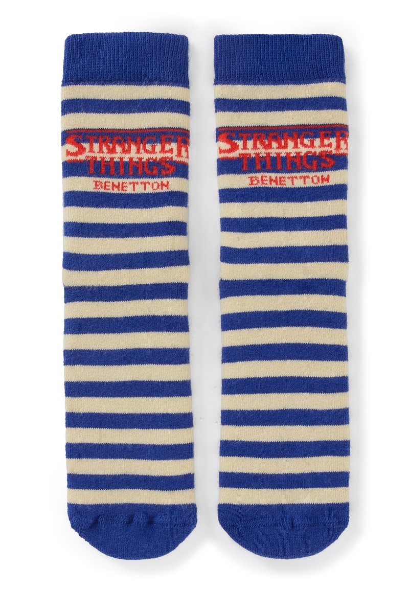 Calzini a righe blu e bianche con logo rosso "Stranger Things Benetton" vicino alla parte superiore, posati distesi affiancati su sfondo bianco.