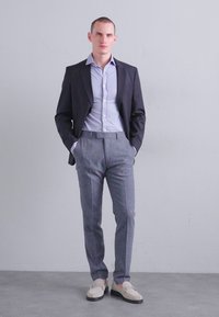 Îmbrăcăminte pentru bărbați care include un sacou negru, o cămașă bleu deschis, pantaloni gri și mocasini bej. Sacoul are rever, iar pantalonii sunt croiți.