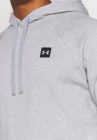 Grå huvtröja med en diskret textur, med en svart logotyp på framsidan och grå dragsnöre.