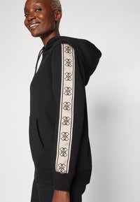 Felpa nera con tasca frontale, caratterizzata da una striscia a motivo beige lungo le maniche. Il materiale sembra morbido e ha una vestibilità comoda.