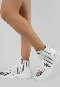 Weiße High-Top-Sneaker mit glitzernden silbernen Streifen und einem roten Akzent, mit einer glatten Textur und einer flachen Gummisohle. Schnürdesign.