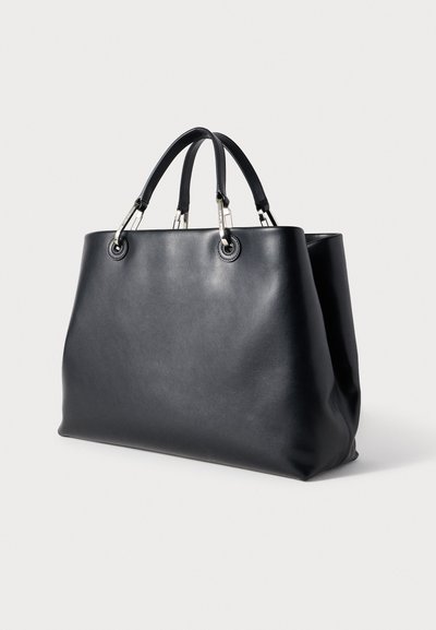 Μαύρη τσάντα tote από δέρμα με δύο επάνω λαβές και ασημένια μεταλλικά στοιχεία. Λείο υλικό, ευρύχωρος σχεδιασμός και στρογγυλεμένες γωνίες.