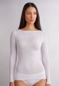 Haut à manches longues blanc en matériau léger et transparent, avec une texture lisse. Présente un décolleté large et un design ajusté.
