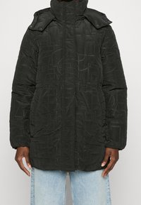 Svart vadderad pufferjacka med hög krage, tryckknappar, elastiska muddar och texturerade mönster. Regular fit, dragsko i midjan för justering.