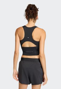 Crna atletska majica bez rukava s izrezom na leđima, uparena s crnim trkaćim kratkim hlačama koje imaju džep na pojasu.