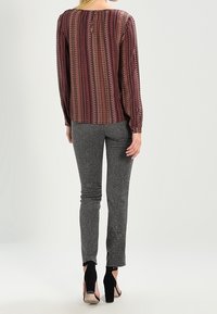 Blusa a maniche lunghe, color bordeaux e crema con motivo a fantasia, abbinata a pantaloni grigi a taglio slim in tessuto testurizzato e scarpe con tacco alto nere.